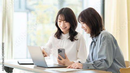 パソコンとスマホを使って話す2人の女性・ビジネスウーマン