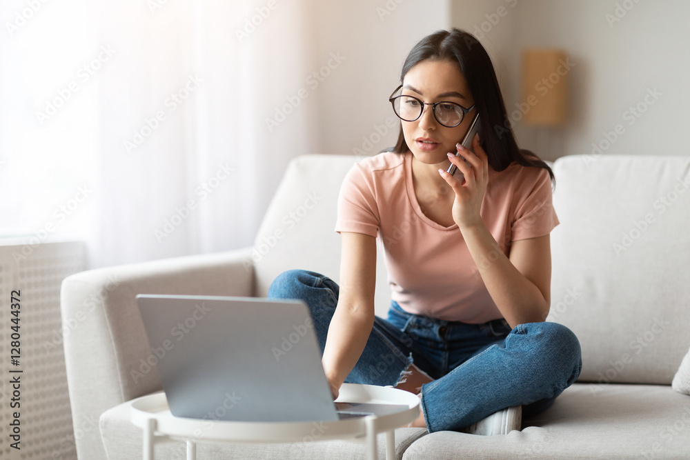 Freelance Career. Girl Working On Laptop Talking On Mobile Phone Sitting On Sofa Indoors. Free Space, Selective Focus Freelance Career. Girl Working On Laptop Talking On Mobile Phone Sitting On Sofa Indoors. Free Space, Selective Focus