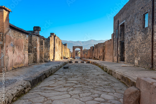 Via Di Mercurio in Pompeii is a main road known in ancient Rome as the cardo maximus. A north-south street that crosses the city. In the background, the Arch of Caligula