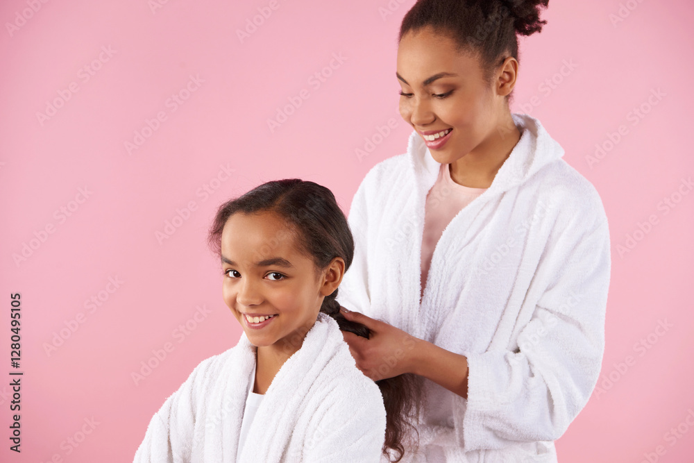 African American mother braids plait of little daughter. Isolated on pink background. African American mother braids plait of little daughter. Isolated on pink background.