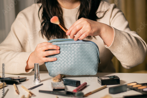Woman putting makeup brushes in blue cosmetic bag. Travel cosmetic bag to go. Beauty concept. Decorative cosmetics