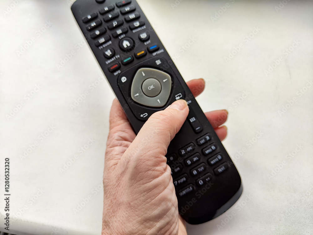 Holding a remote control while sitting at a table with a light surface in a casual indoor setting
