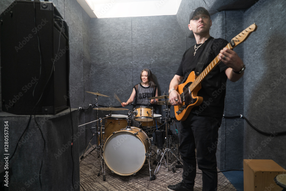 Fototapeta premium guitarist and female drummer playing together in professional soundproof rehearsal studio. Rock band members practicing live performance and sound arrangement.