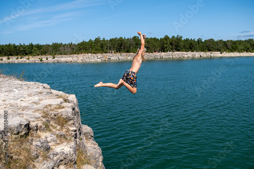 Shirtless boy diving with arms raised in lake photo