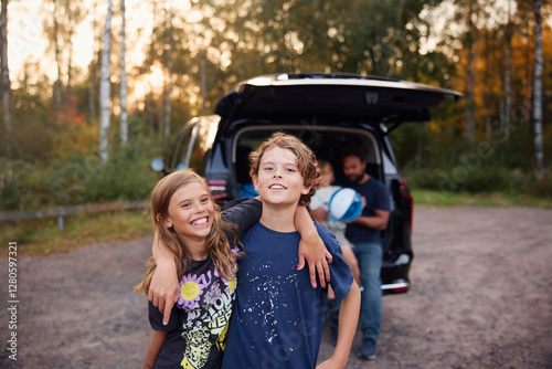 Portrait of smiling girl standing with arm around brother in forest