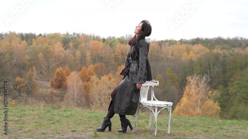 Fall nature landscape and girl. Central park in New York. Girl in fall trench. Autumn landscape with gothic woman on chair. Stylish woman and chair in autumn landscape outdoor. Graceful silhouette