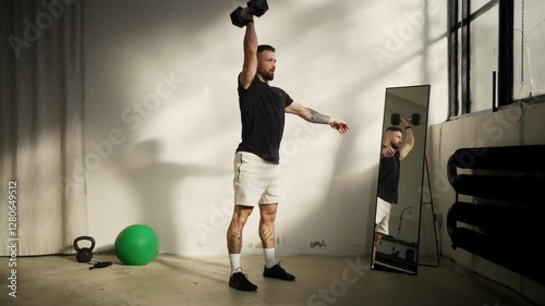An athletic man is skillfully doing a dumbbell shoulder press in a modern gym