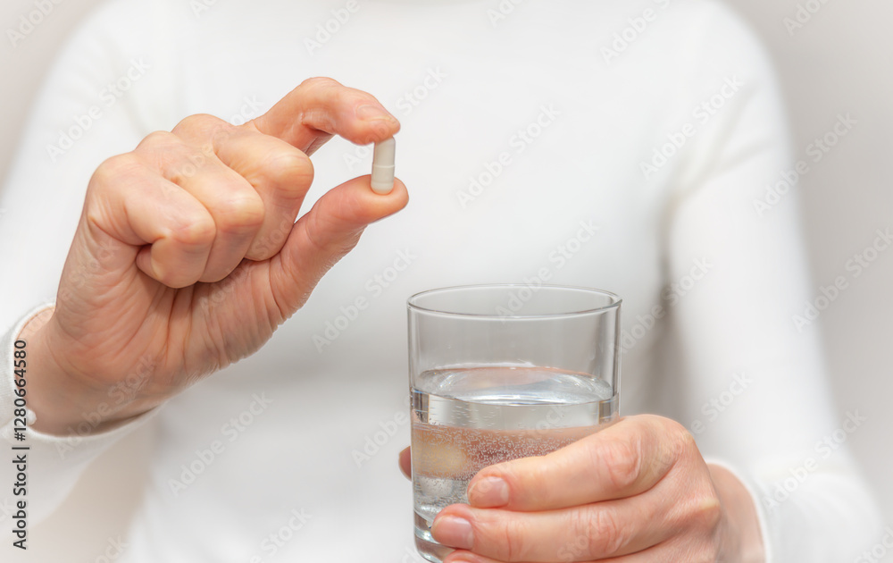 Woman prepares to take a capsule with a glass of water indoors in a bright setting