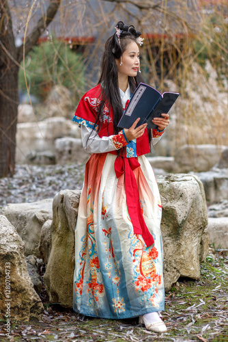 Fotografía A young Asian woman in a traditional red Chinese costume walks in the park, reads national haiku poetry