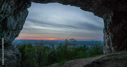 Witness the breathtaking beauty of a sunset over a city timelapse captured through a large cave arch.