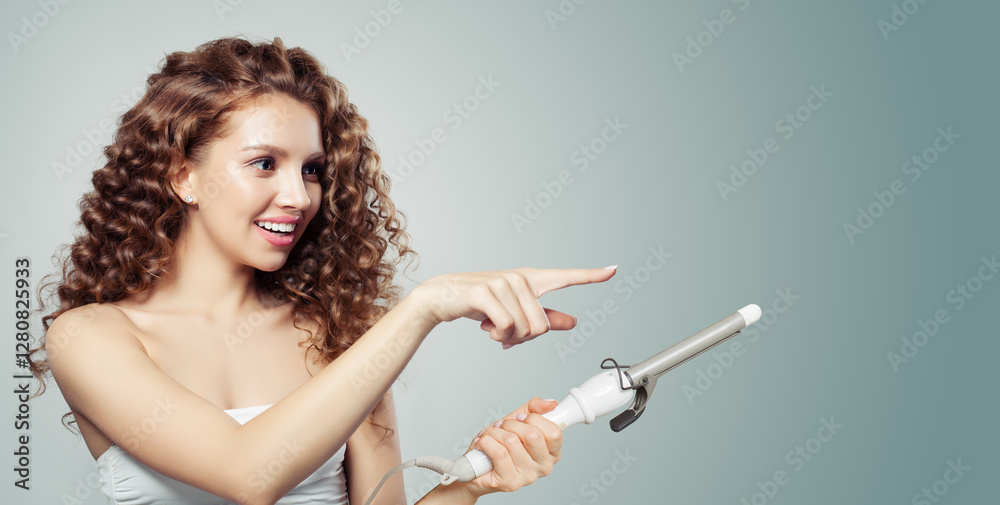 Obraz premium Fashion portrait of brunette model using curling iron on grey background. Coiffure, beauty salon and hair styling concept