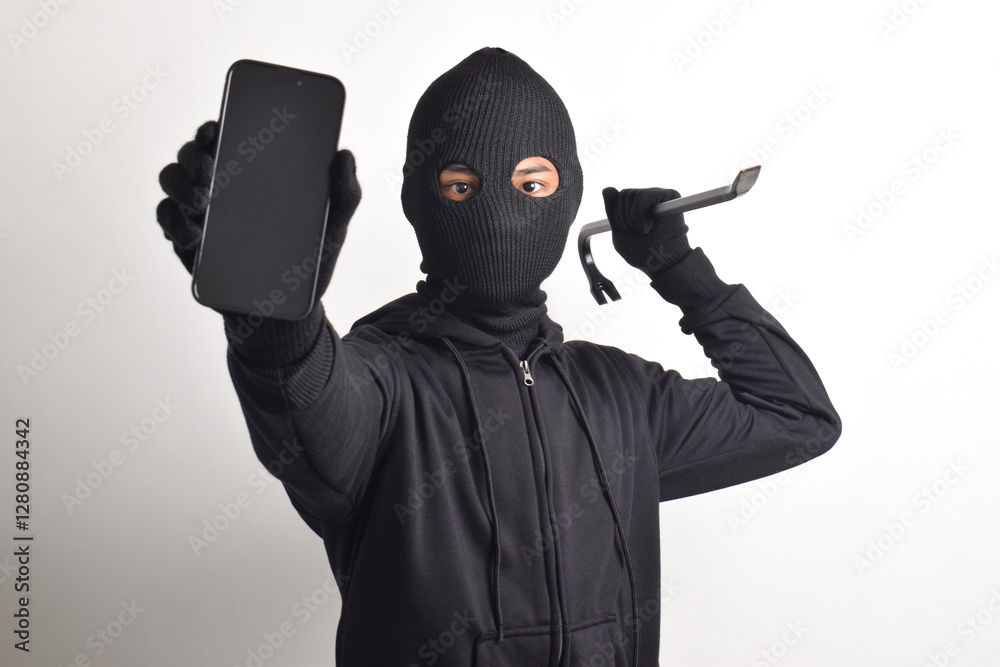 Mysterious man wearing black hoodie and mask doing hacking activity on mobile phone, hacker holding smartphone and crowbar, isolated on white background. Mysterious man wearing black hoodie and mask doing hacking activity on mobile phone, hacker holding smartphone and crowbar, isolated on white background.
