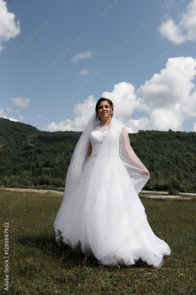 a woman in a wedding dress stands in an open field. She is wearing a white dress with lace elements and a long veil. She has dark hair tied up in an updo. a woman in a wedding dress stands in an open field. She is wearing a white dress with lace elements and a long veil. She has dark hair tied up in an updo.