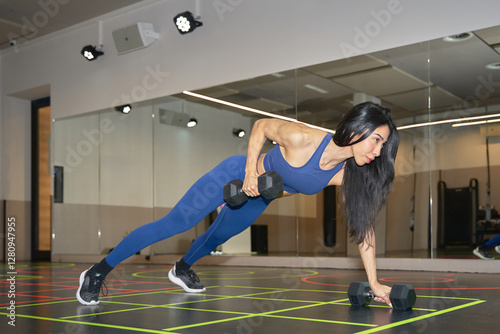 Determined sportswoman doing renegade rows with dumbbells in gym