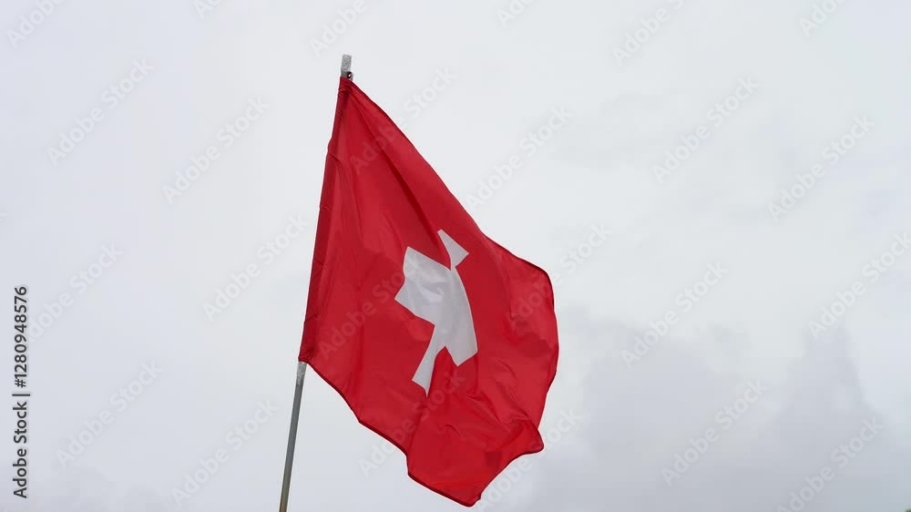 The Swiss flag waves in the breeze on a cloudy day, symbolizing national pride and identity amidst a moody sky.