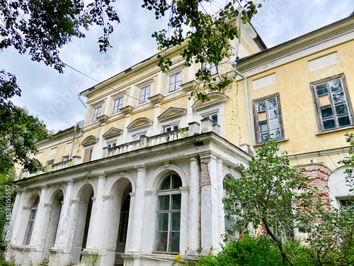 Canvas Print The building of an old manor is white with peeling plaster against a background of green trees on a clear sunny day