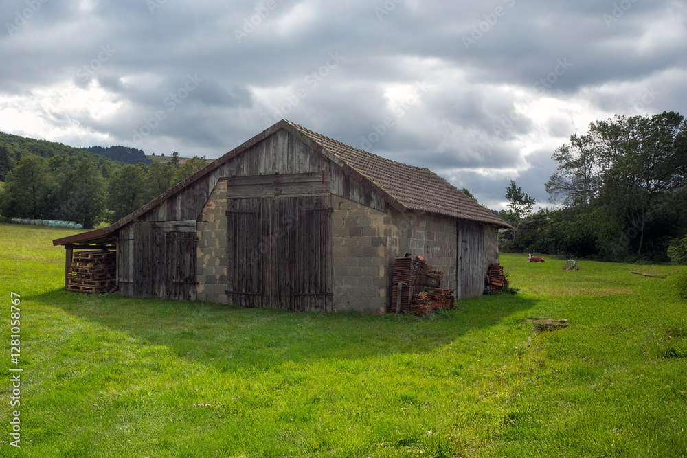 A rustic barn stands in an expansive green field, under a cloudy sky, showcasing a peaceful rural setting that evokes nostalgia and simplicity in nature.