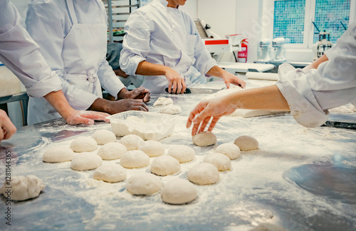 Hands of baking students working with fresh dough in a professional kitchen. Artisan bread preparation, teamwork, and pastry training in a culinary school. Flour, dough balls, and rolling techniques.
