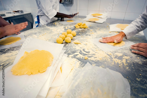 Students in a bakery school flattening dough balls by hand on a floured stainless steel table. Hands-on pastry training in a professional kitchen, learning traditional baking techniques.