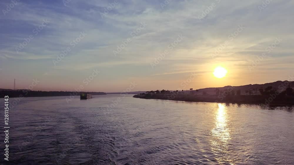 A golden sunset reflects on the tranquil waters of the Nile River, blending seamlessly with the sky. A cruise ship glides through the river. A serene and picturesque journey, Aswan to Luxor, Egypt. A golden sunset reflects on the tranquil waters of the Nile River, blending seamlessly with the sky. A cruise ship glides through the river. A serene and picturesque journey, Aswan to Luxor, Egypt.