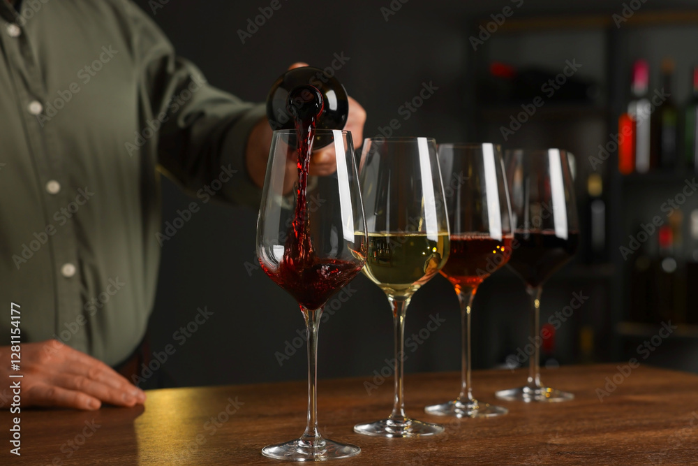 Professional sommelier pouring red wine into glasses on wooden table indoors, closeup