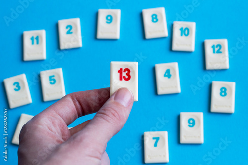 Fotografie hand holding a chip with red number 13 with other blue numbers on the background