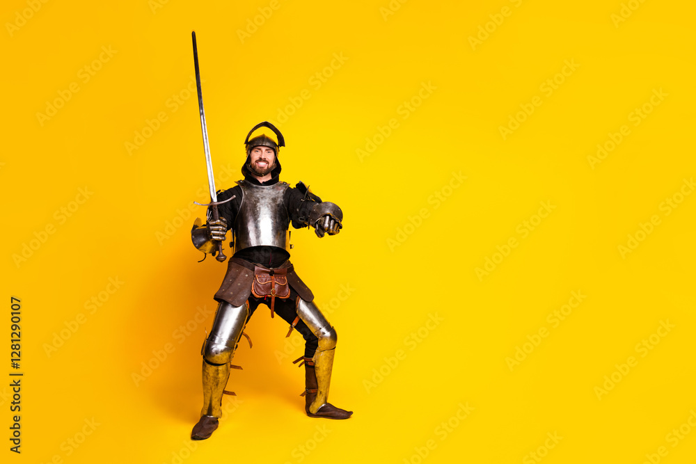 Young man dressed as a medieval knight with a sword on yellow background Young man dressed as a medieval knight with a sword on yellow background