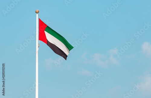 Waving national flag of United Arab Emirates on flagpole, set against a vibrant blue sky, symbolizes pride and identity of the nation