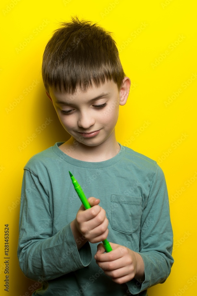 Curious child holding a green marker, smiling thoughtfully against a vibrant yellow background, wearing a teal shirt. Curious child holding a green marker, smiling thoughtfully against a vibrant yellow background, wearing a teal shirt.
