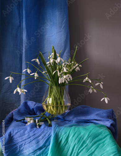 A Beautiful Arrangement of Elegant Snowdrops in a Glass Vase Surrounded by Colorful Textiles