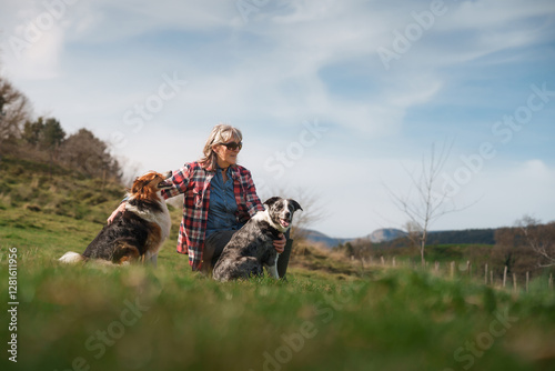 Photography Female farmer kneeling in grassland with two dogs enjoying sunny day