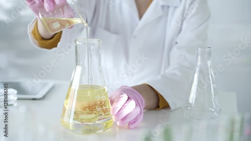 Wallpaper Mural Unknown scientist wearing a lab coat, pink gloves, and a mask is pouring a yellow oily liquid from one beaker to another in a laboratory setting, close up. Science and medicine Torontodigital.ca