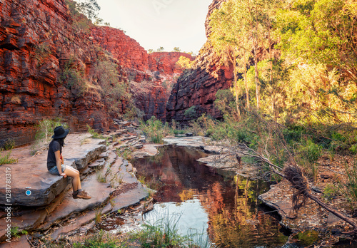 woman sitting on rocks in gorge at Karijini National Park, Western Australian wearing hat and boots photo