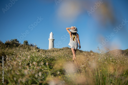 woman walking up hill to lighthouse with shrubs and blue sky
