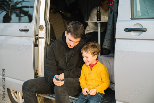 Father and son enjoying camper van life, watching smartphone together