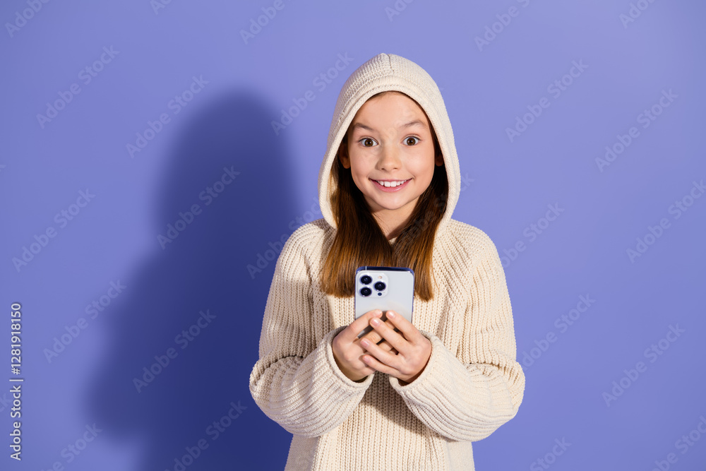 Φωτογραφία Adorable young girl in casual hoodie excitedly holding smartphone on vivid purpl