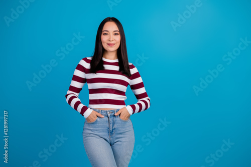 Smiling young woman against blue background dressed casually in striped shirt showcasing cheerful and stylish demeanor photo