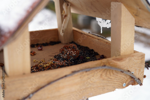 A close-up photo of a bird feeder containing birdseed and a suet ball.
