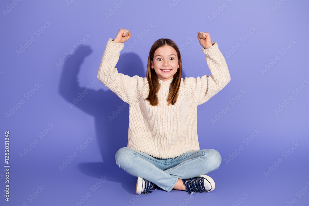 Cute girl sitting on purple background with an excited expression and raised joyful arms, wearing stylish casual pullover and jeans. Cute girl sitting on purple background with an excited expression and raised joyful arms, wearing stylish casual pullover and jeans.