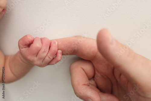Close-up little hand of child and palm of mother and father. The newborn baby has a firm grip on the parent's finger after birth. A newborn holds on to mom's, dad's finger. 