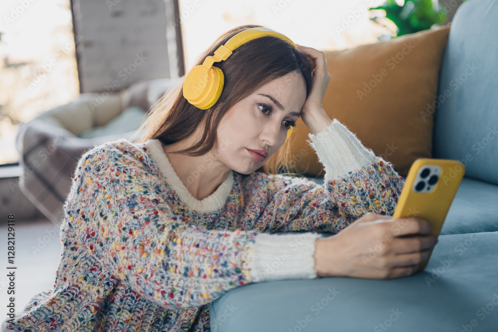Φωτογραφία Young woman with yellow headphones holding smartphone indoors in casual sweater