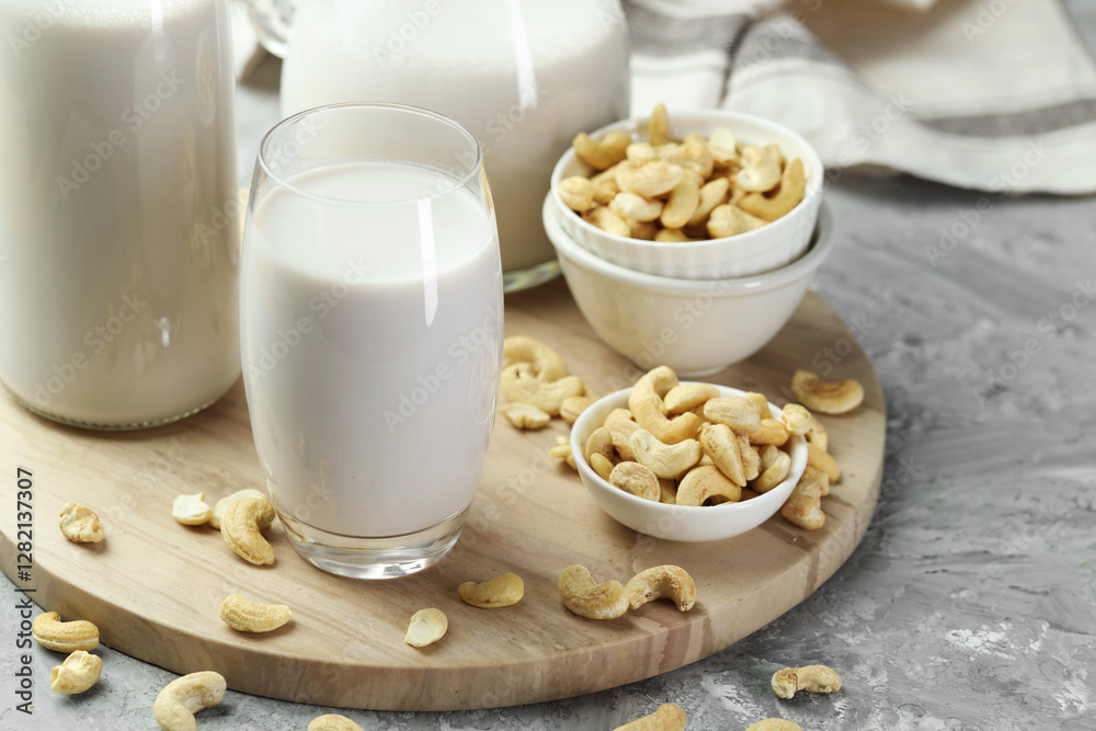 Glassware with fresh cashew milk and nuts on grey table, closeup Glassware with fresh cashew milk and nuts on grey table, closeup