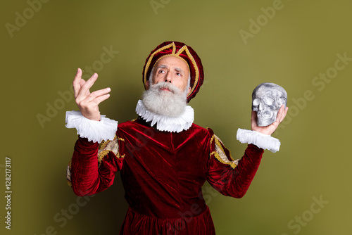 Mature man in a costume holding a skull on khaki background demonstrating historic and expressive style, think to be or not to be photo