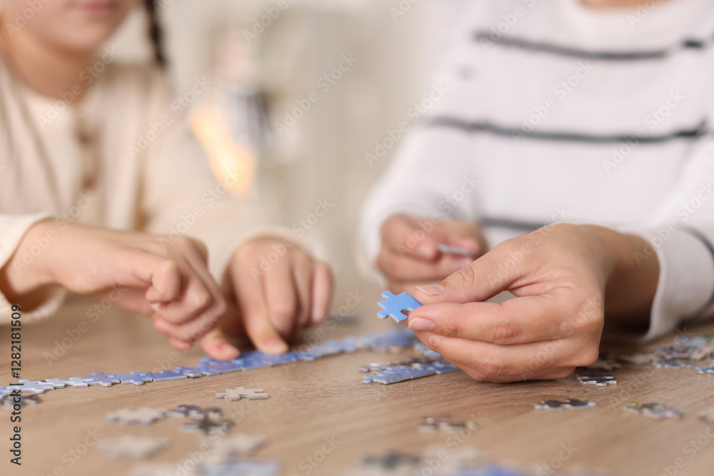 Mother and her daughter solving puzzle together at wooden table indoors, closeup Mother and her daughter solving puzzle together at wooden table indoors, closeup