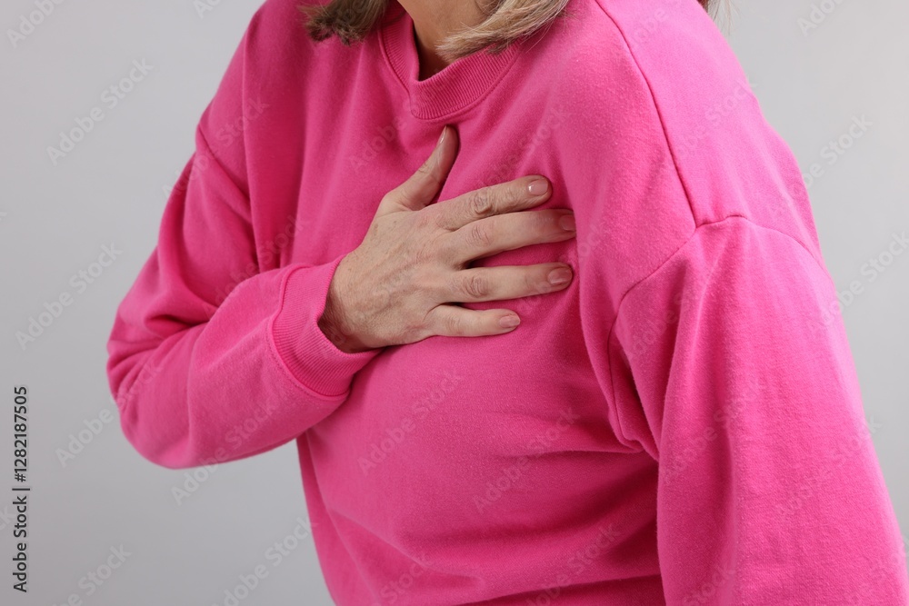 Heart attack. Senior woman suffering from pain in chest on light grey background, closeup Heart attack. Senior woman suffering from pain in chest on light grey background, closeup