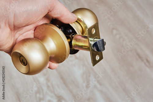 Technical view of a brass doorknob with its internal locking system exposed, hands manipulating the knobs for demonstration or repair work.