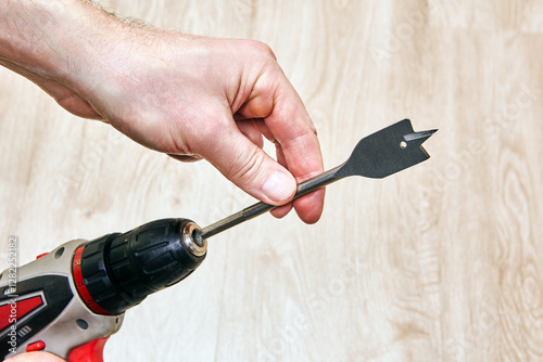 Cordless drill with spade bit held by hand.