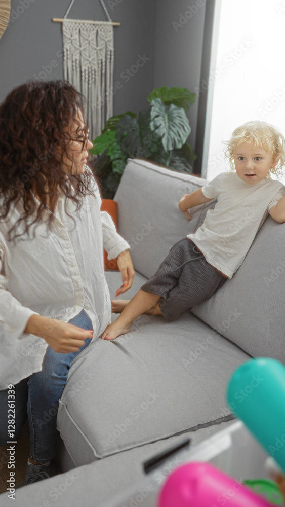 Obraz premium Woman interacting with young boy in modern living room highlights family bond with relaxed atmosphere and natural light surrounding them in a cozy, stylish apartment setting.