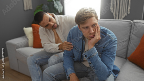 Two men indoors in a living room, one consoling the other who looks upset, highlighting their adult friendship and emotional relationship in a home setting.