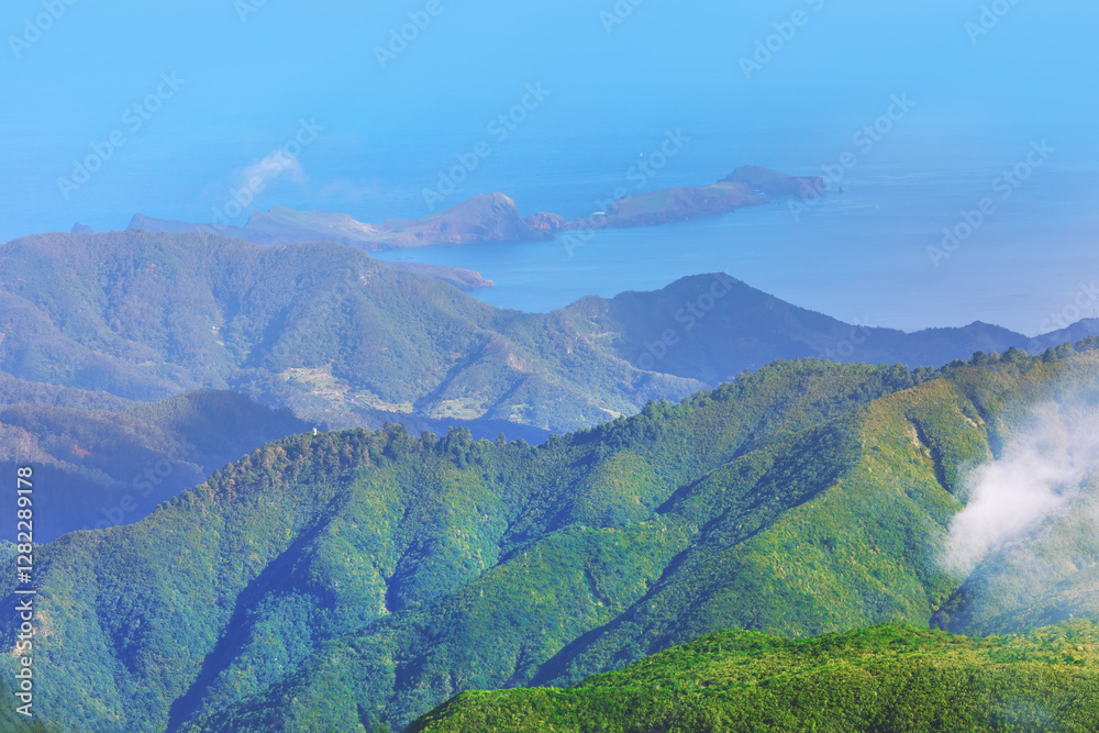 Breathtaking view of Madeira rugged mountains covered in lush greenery, stretching towards deep blue Atlantic Ocean. Remote landscape and misty atmosphere highlight island wild and untouched beauty